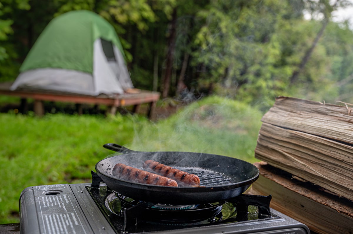 Camco Deluxe Folding Grill Table set up at a campsite with stove and cooking supplies