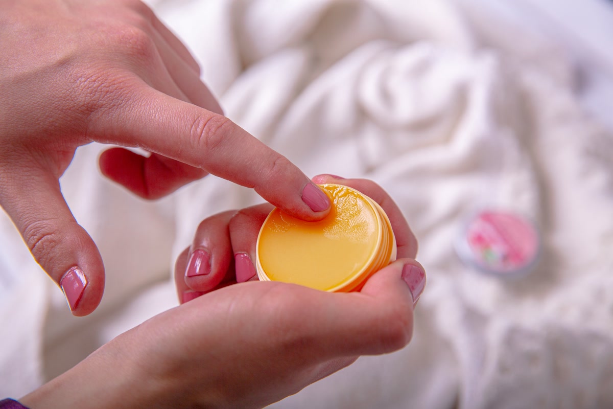 A close-up of a dog's pink nose being gently moisturized with a balm, the product being applied with care, soft natural lighting, detailed texture of the dog's nose
