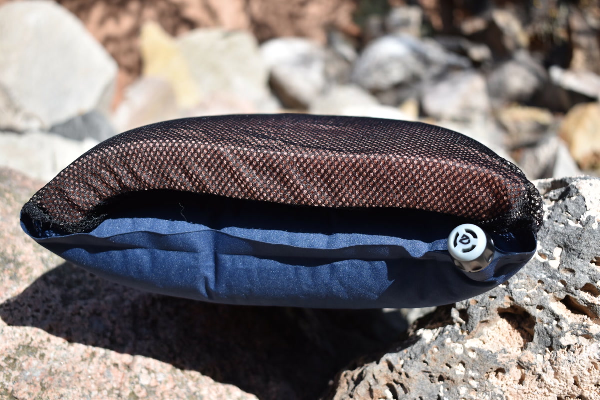 Photograph of a Nemo Fillo camping pillow resting on a sleeping pad inside a tent, with a rainfly visible through the mesh ceiling and a headlamp nearby