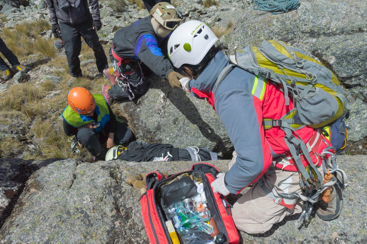 Compact red first aid pouch attached to a hiking backpack with dog gear on a mountain trail