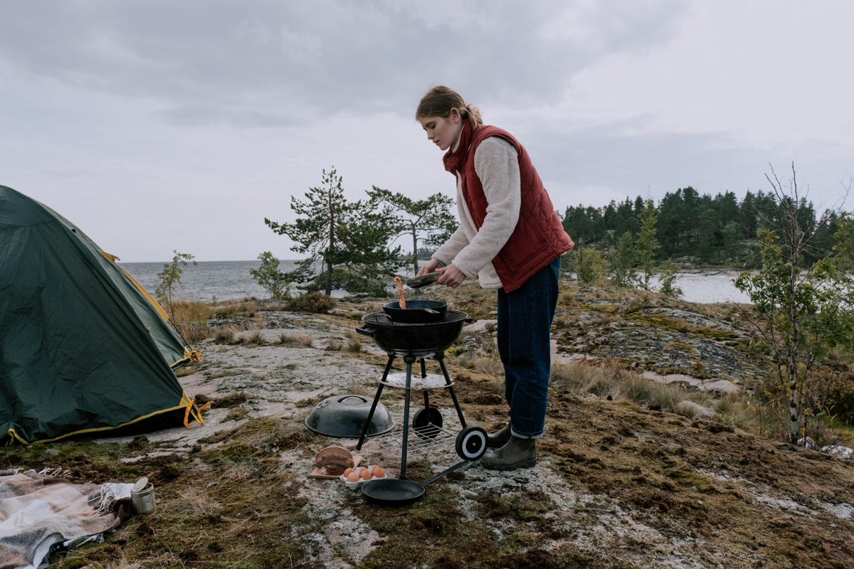 Person cooking on a portable grill at a campsite near a tent