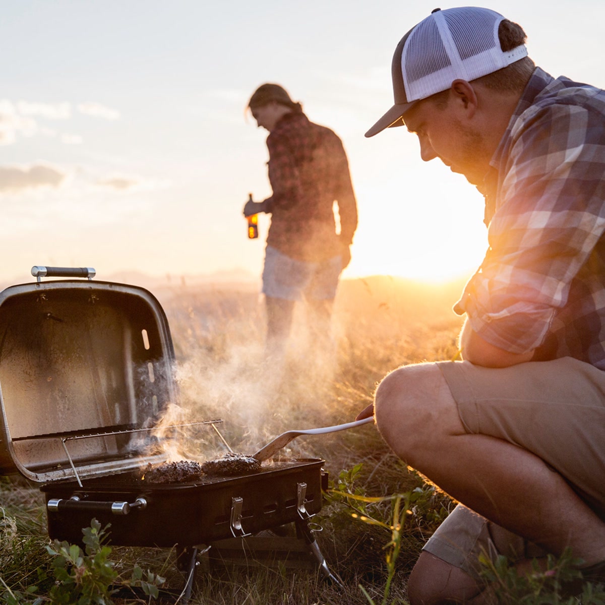 Camp chef flipping burgers on a portable grill at a campsite