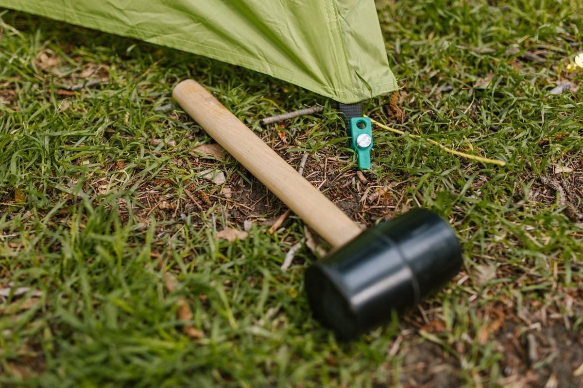 Y-shaped aluminum tent stakes driven into forest soil next to a camping tent
