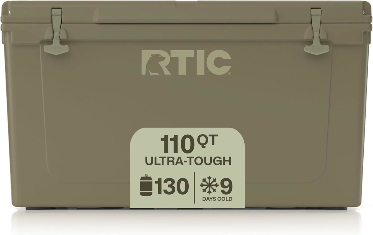 RTIC 45qt hard cooler in white sitting on a picnic table at a lakeside campsite, surrounded by campi